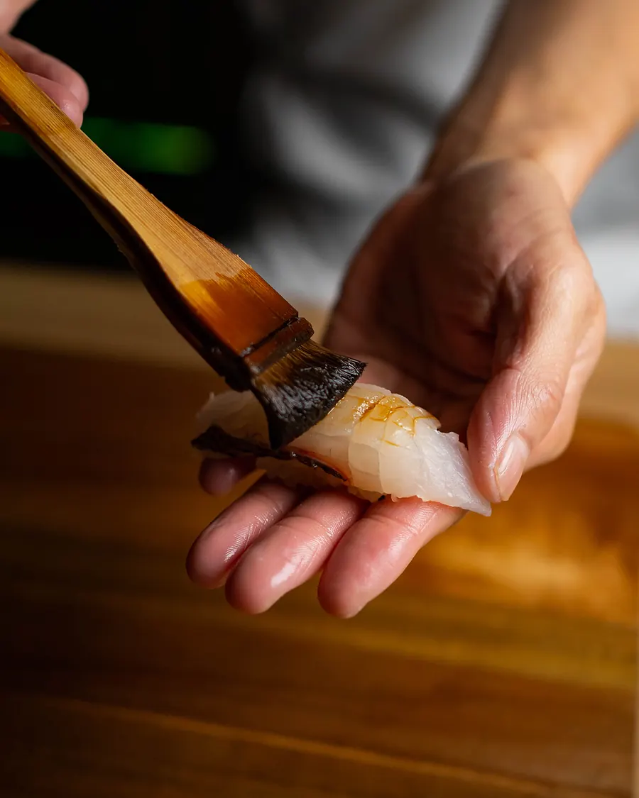 A chef's hands brushing sauce onto nigiri