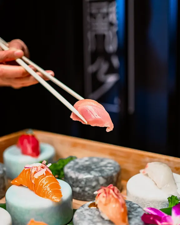 Nigiri lifted with chopsticks from stone stands