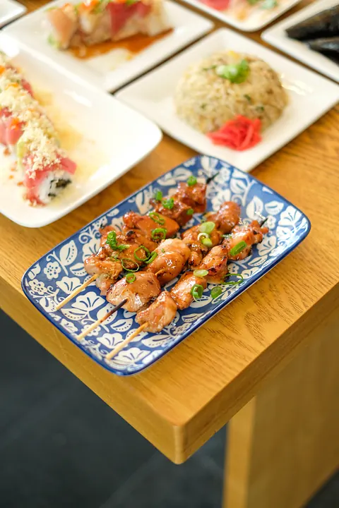 Skewers on a blue plate next to sushi rolls
