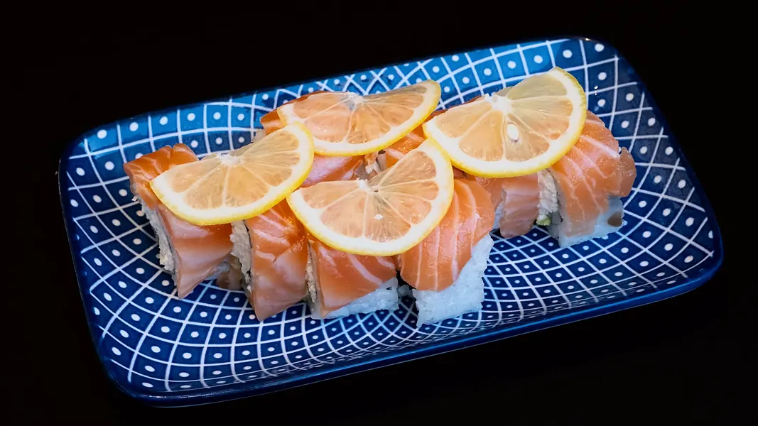 A roll topped with salmon and lemon on a blue plate